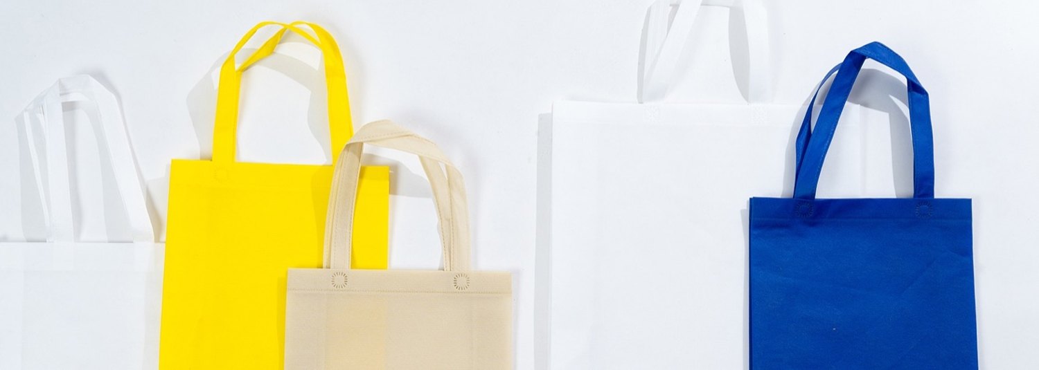 Five plain non woven tote bags in white, yellow, cream and blue, standing upright